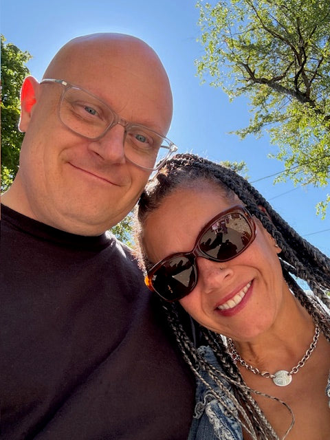 Two people posing for a photo outdoors with trees and blue sky in the background.